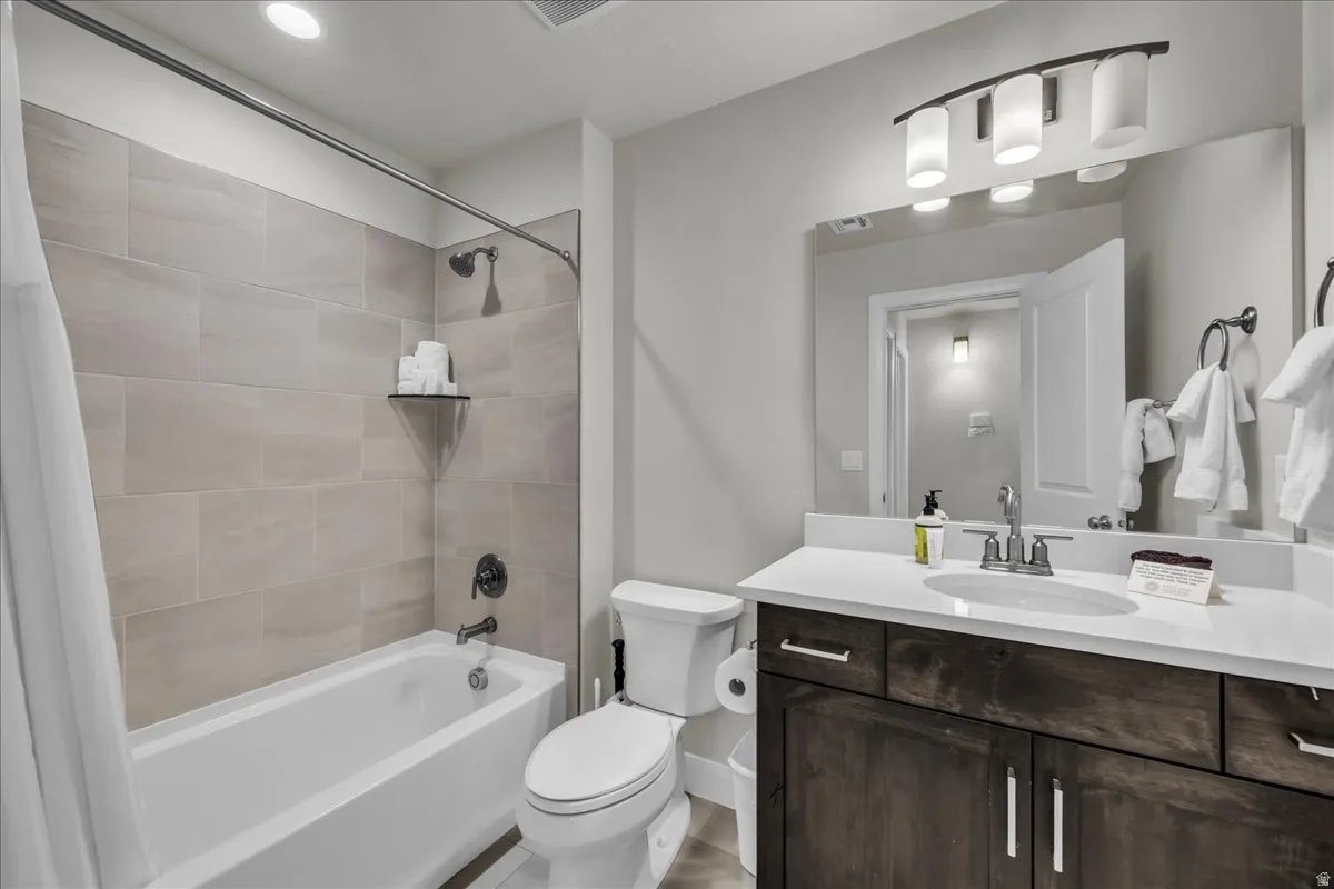 Bathroom featuring a white bathtub with subway tile surround, a built-in shower shelf, a dark wood-finish vanity with a white countertop, and a vanity mirror with overhead lighting