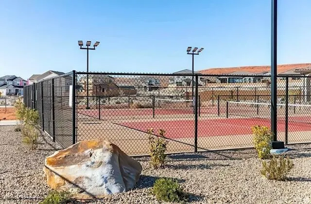 Fenced outdoor court with red playing surface, white boundary lines, and permanent net