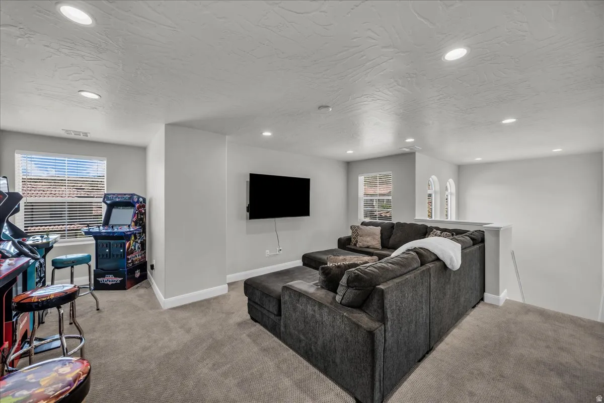 Carpeted entertainment area featuring recessed lighting, multiple windows with blinds, and a partial wall with decorative arched cutouts