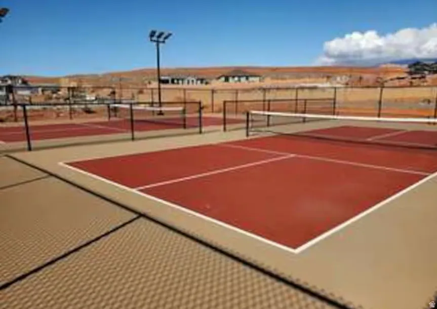 Red hard court surface with white boundary lines and perimeter fencing