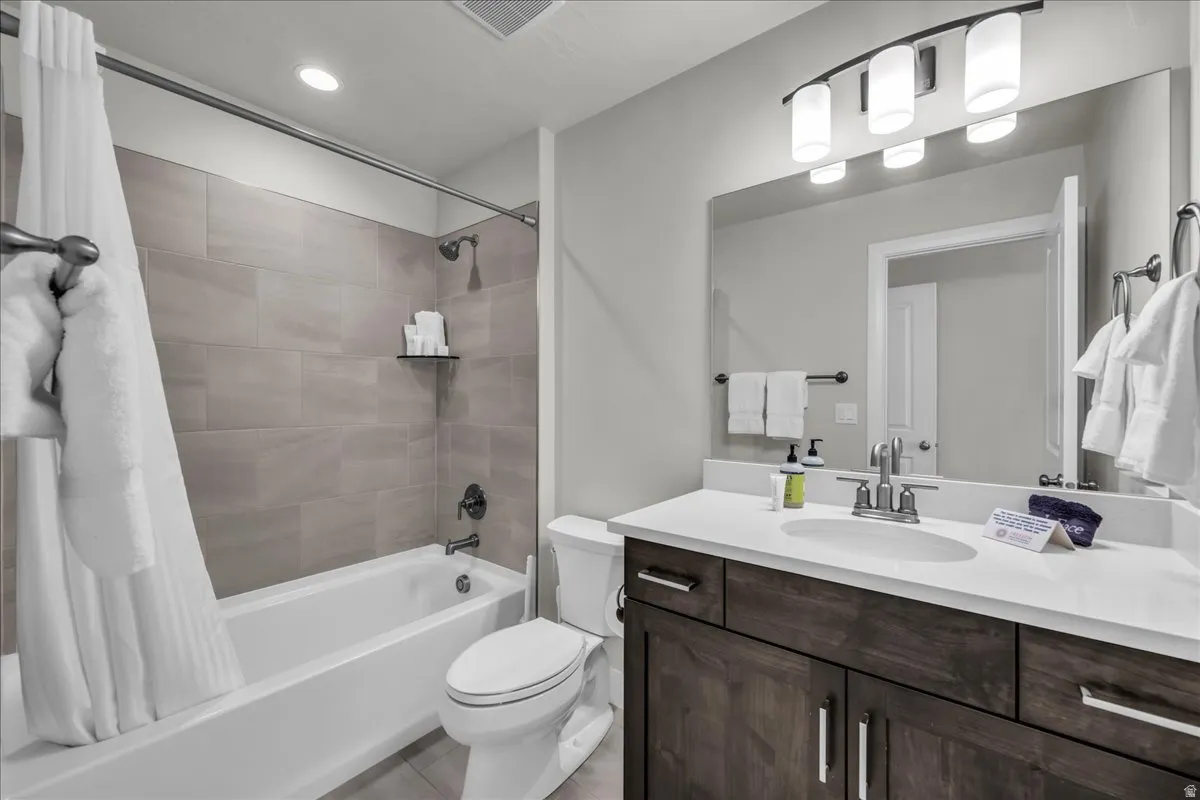 Full bathroom with a white tub-shower combination, light gray tiled shower surround, recessed lighting, and a dark wood-finish vanity with a white countertop