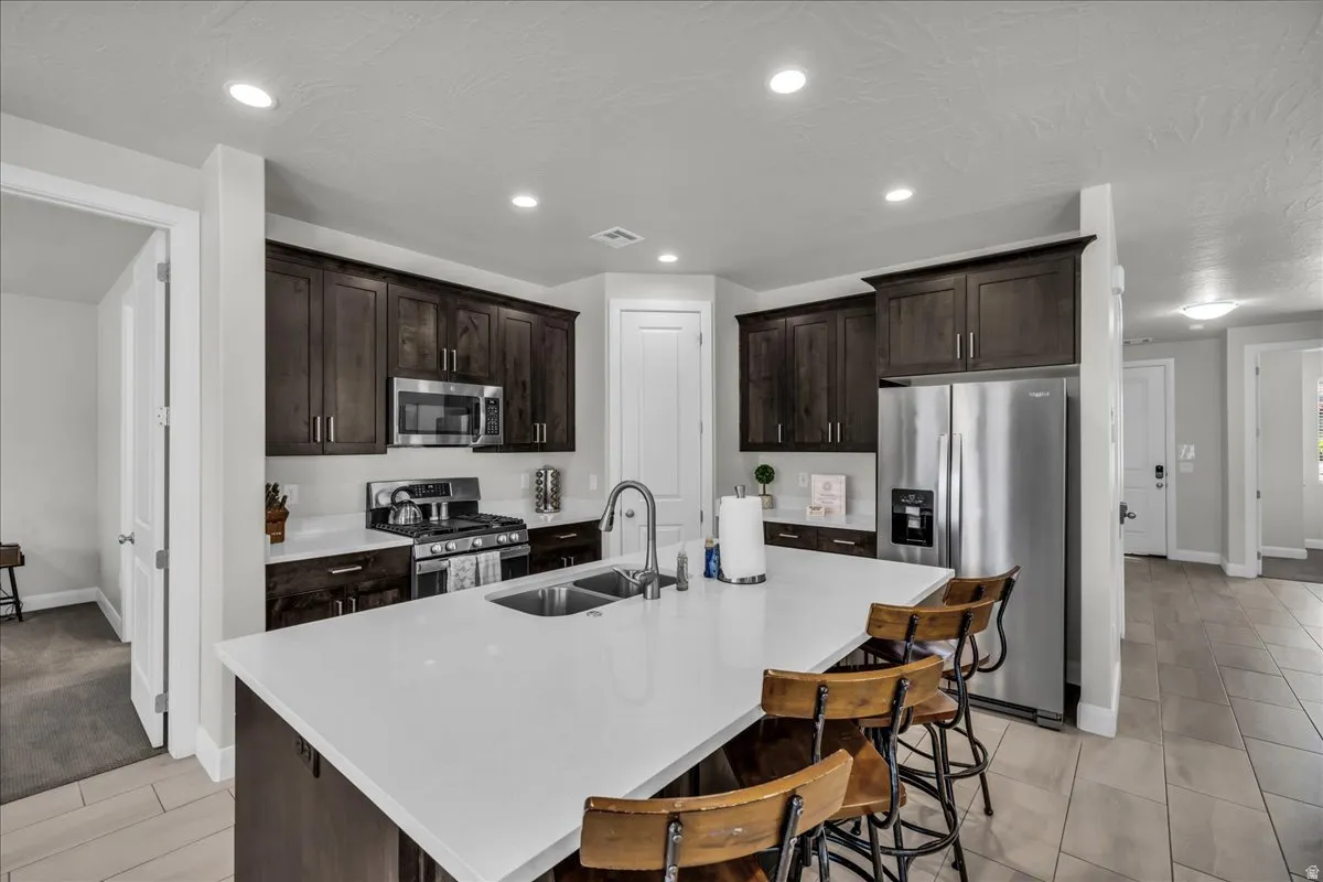 Open-concept kitchen featuring an oversized island with countertop seating, dark wood cabinetry, white countertops, and stainless steel appliances
