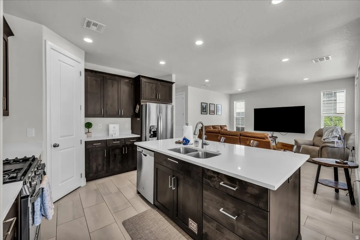 Spacious kitchen featuring an expansive center island with dual sinks, dark wood cabinetry, white countertops, and stainless steel appliances
