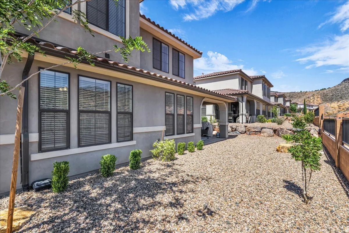 Stucco exterior featuring multiple windows with blinds, a covered patio, and a low-maintenance gravel landscaping