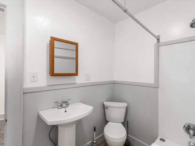 Bathroom featuring a pedestal sink, wall-mounted medicine cabinet with a wood-finish frame, and wainscoting with a two-tone paint scheme