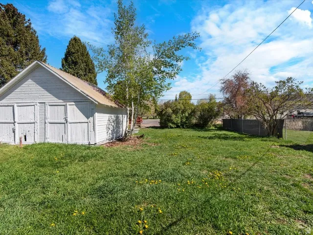 Detached outbuilding with multiple access doors, featuring horizontal wood siding, a sloped roof, and mature trees nearby