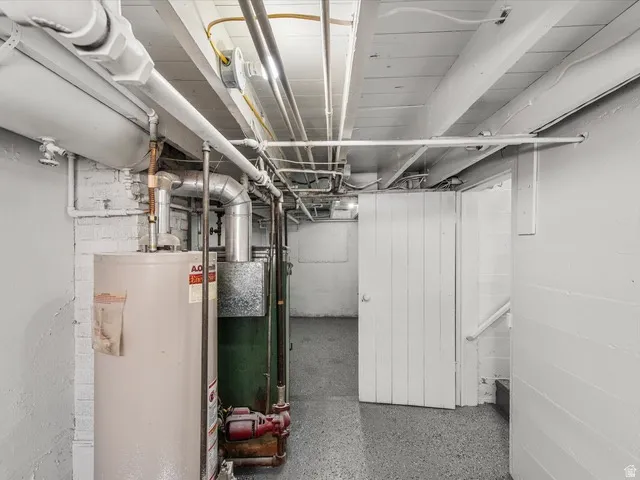 Utility area featuring a water heater, furnace system, painted concrete floors, exposed ceiling joists, and a white paneled door