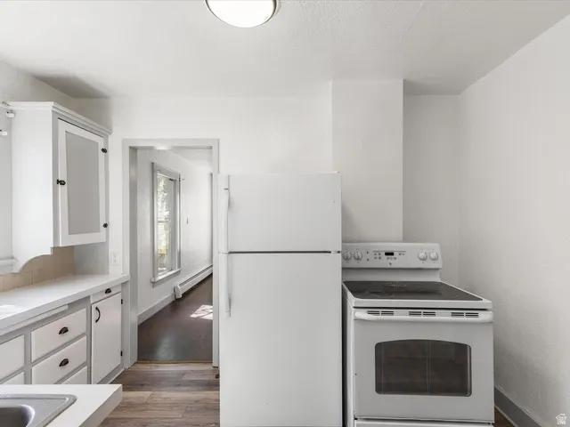 Kitchen featuring white appliances, upper and lower cabinetry with dark hardware, a single basin sink, and wood-finish flooring