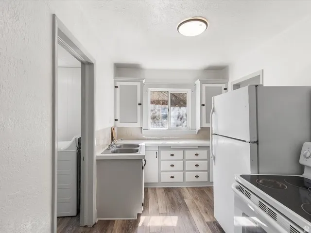 Kitchen featuring wood-finish flooring, white cabinetry, a double basin sink, and a window above