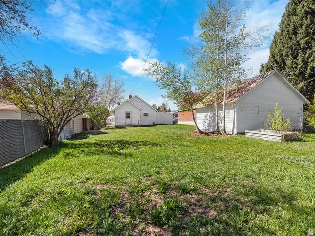 Expansive grassy yard with chain-link fencing, mature trees, and two white auxiliary structures