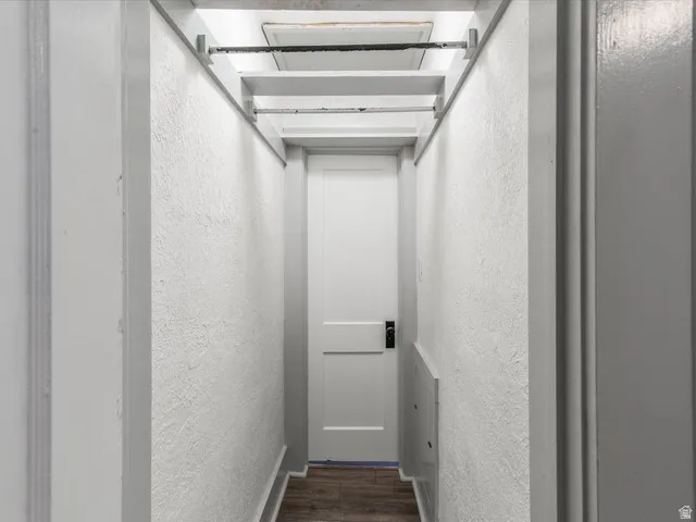 Hallway with white textured walls, wood-finish flooring, and a white interior door with dark hardware