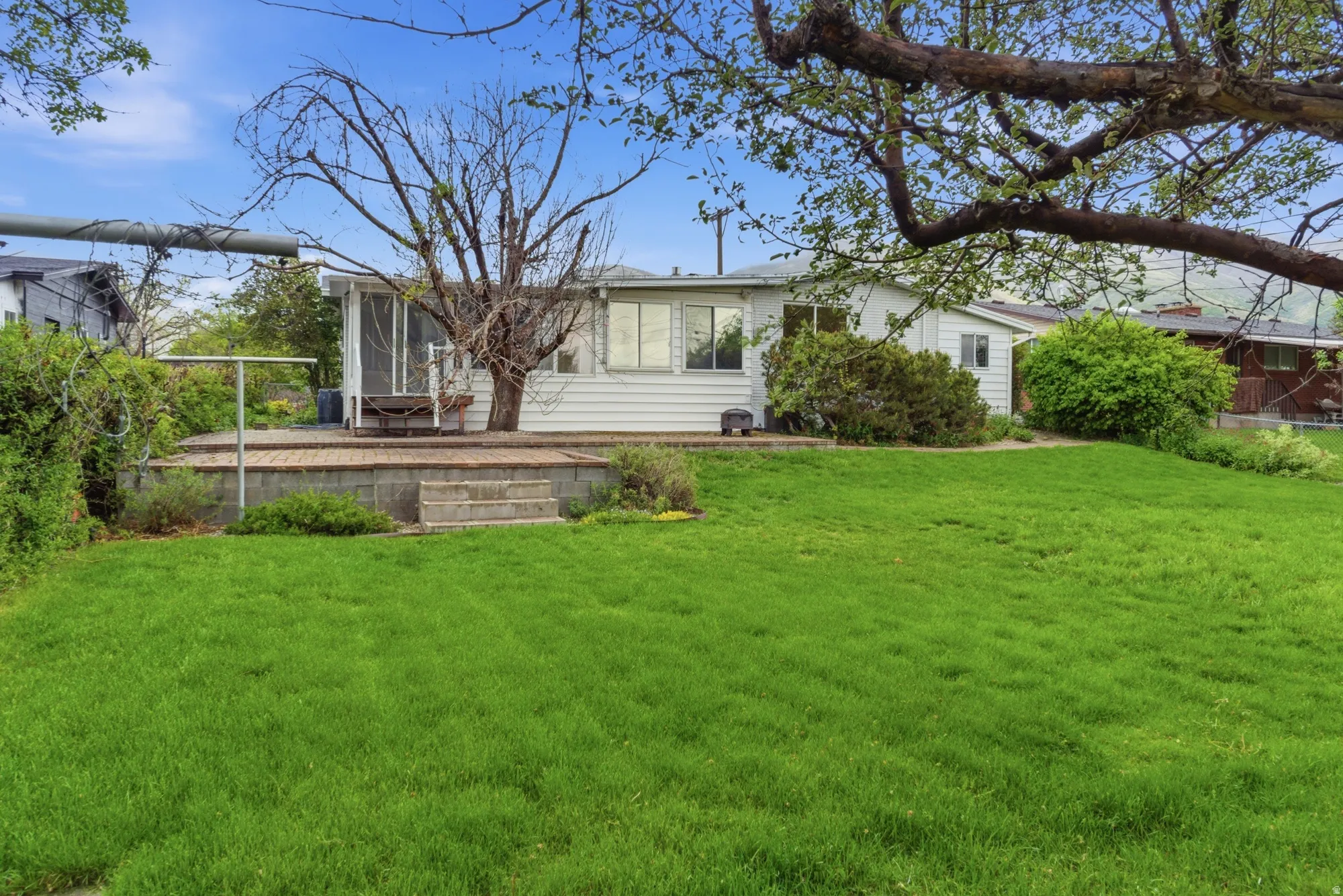 Expansive rear yard featuring a verdant lawn and a raised block patio with steps