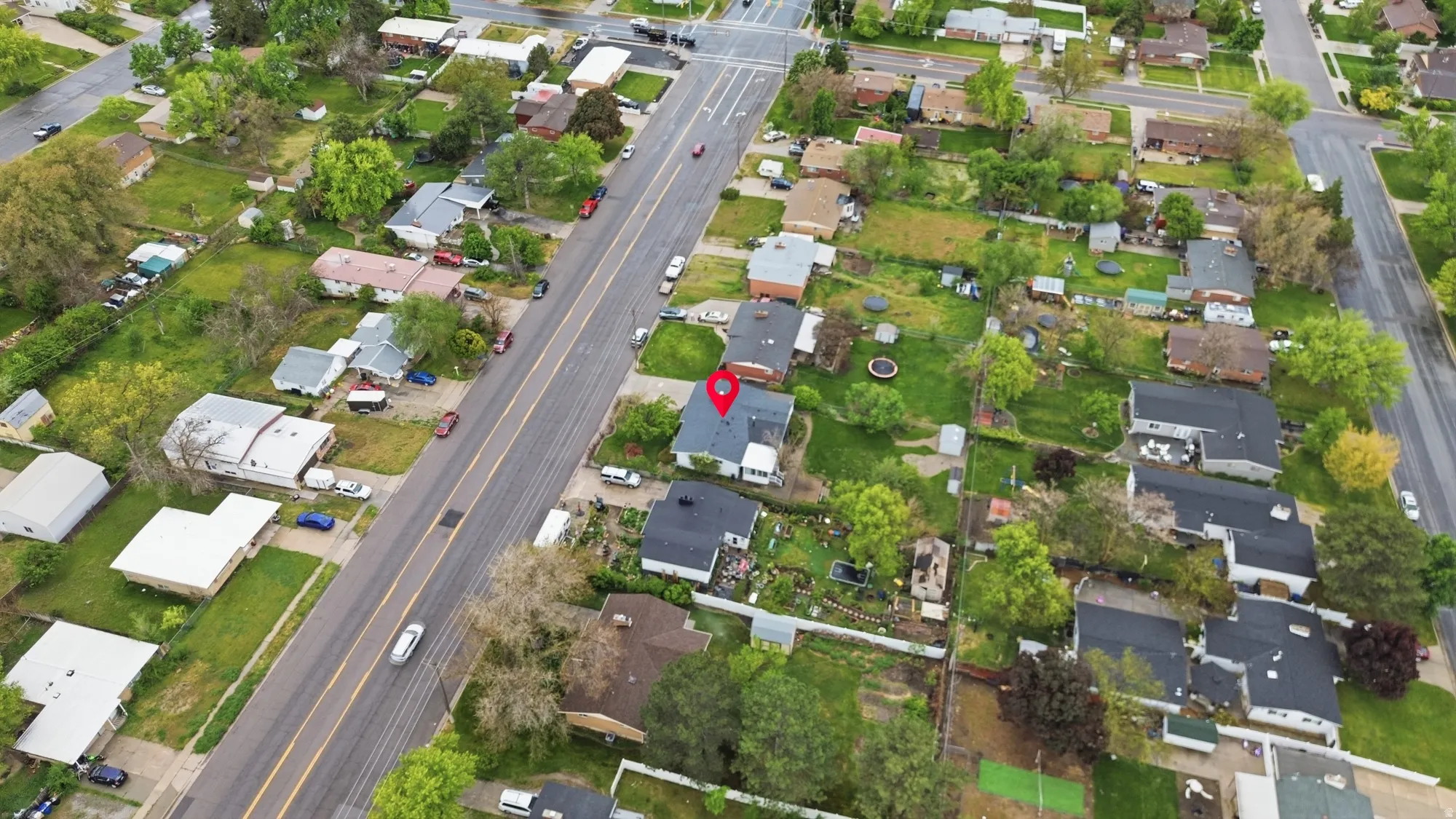 Aerial property overview featuring an asphalt shingle roof, mature perimeter trees, and a spacious backyard with green space