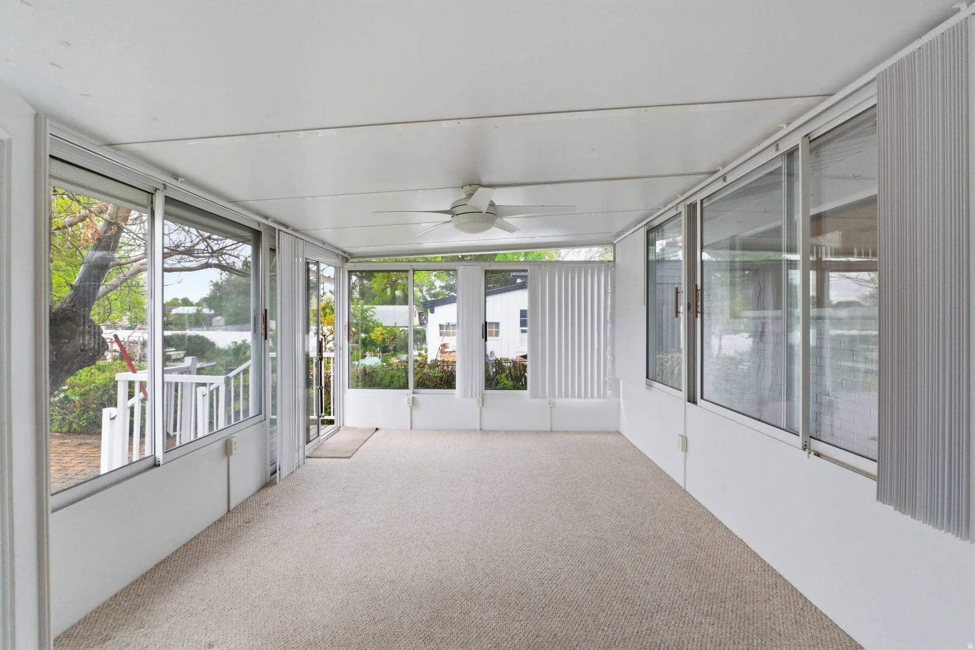 Enclosed patio featuring light-colored carpeting, white paneled walls, and a white ceiling with a ceiling fan