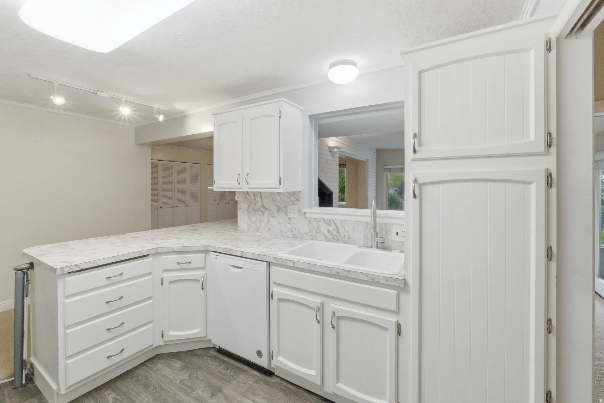 White cabinetry with panel detailing, marble-patterned countertops and backsplash, integrated double basin sink with chrome faucet, built-in dishwasher, and wood-finish flooring