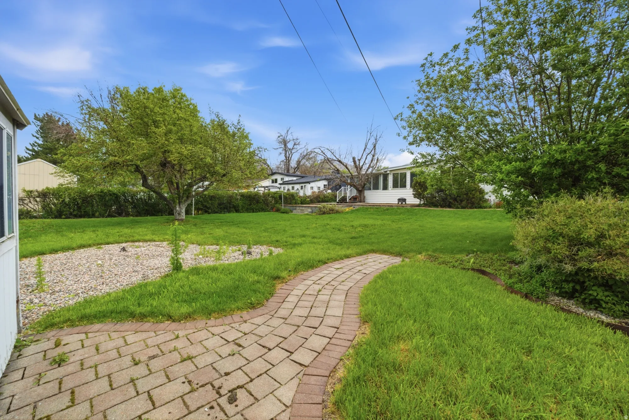 Expansive rear yard featuring a paved brick pathway, a large mature tree, established green lawn, and a decorative gravel bed