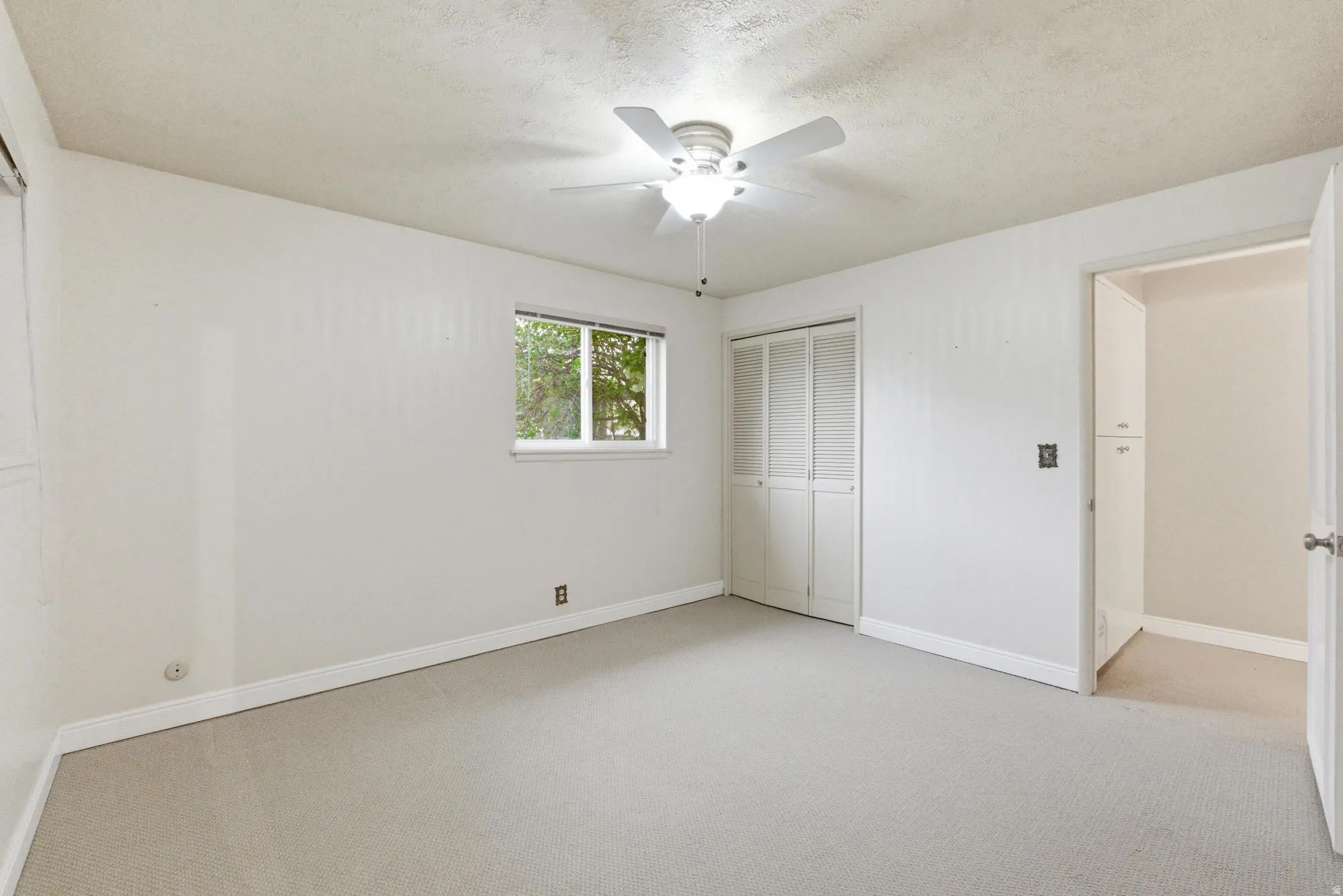 Carpeted room with a ceiling fan, a window, bifold closet doors, and an open doorway revealing built-in cabinetry