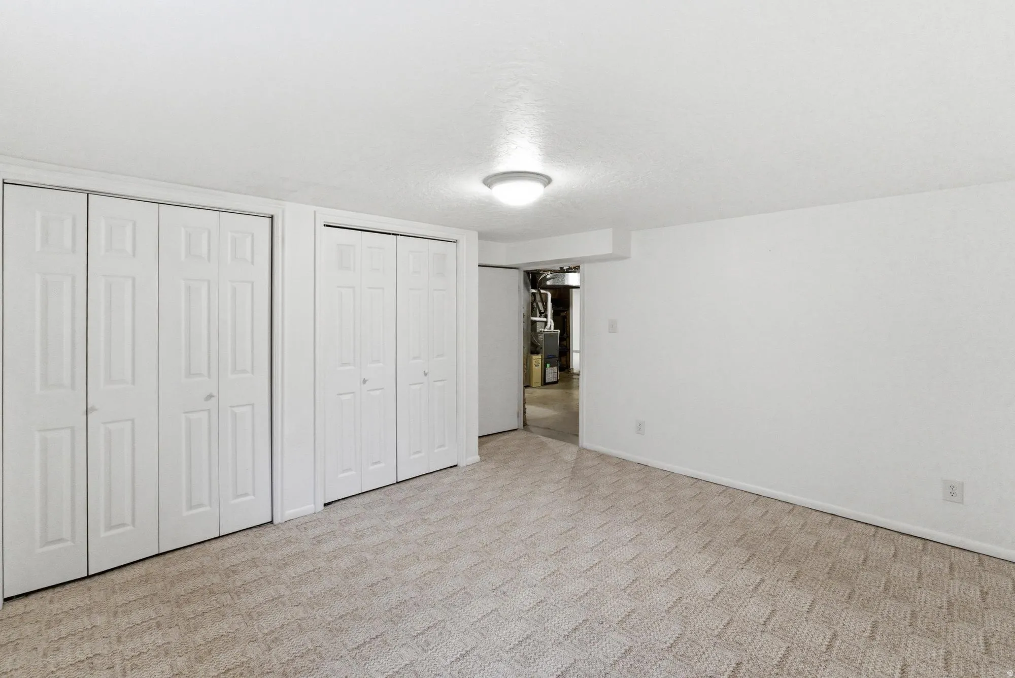 Carpeted room featuring multiple bifold closet doors, a flush-mount ceiling light fixture, and white painted walls