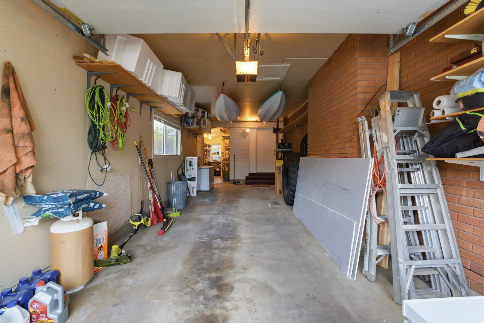 Attached garage with concrete flooring, exposed brick wall, built-in shelving, and a single window