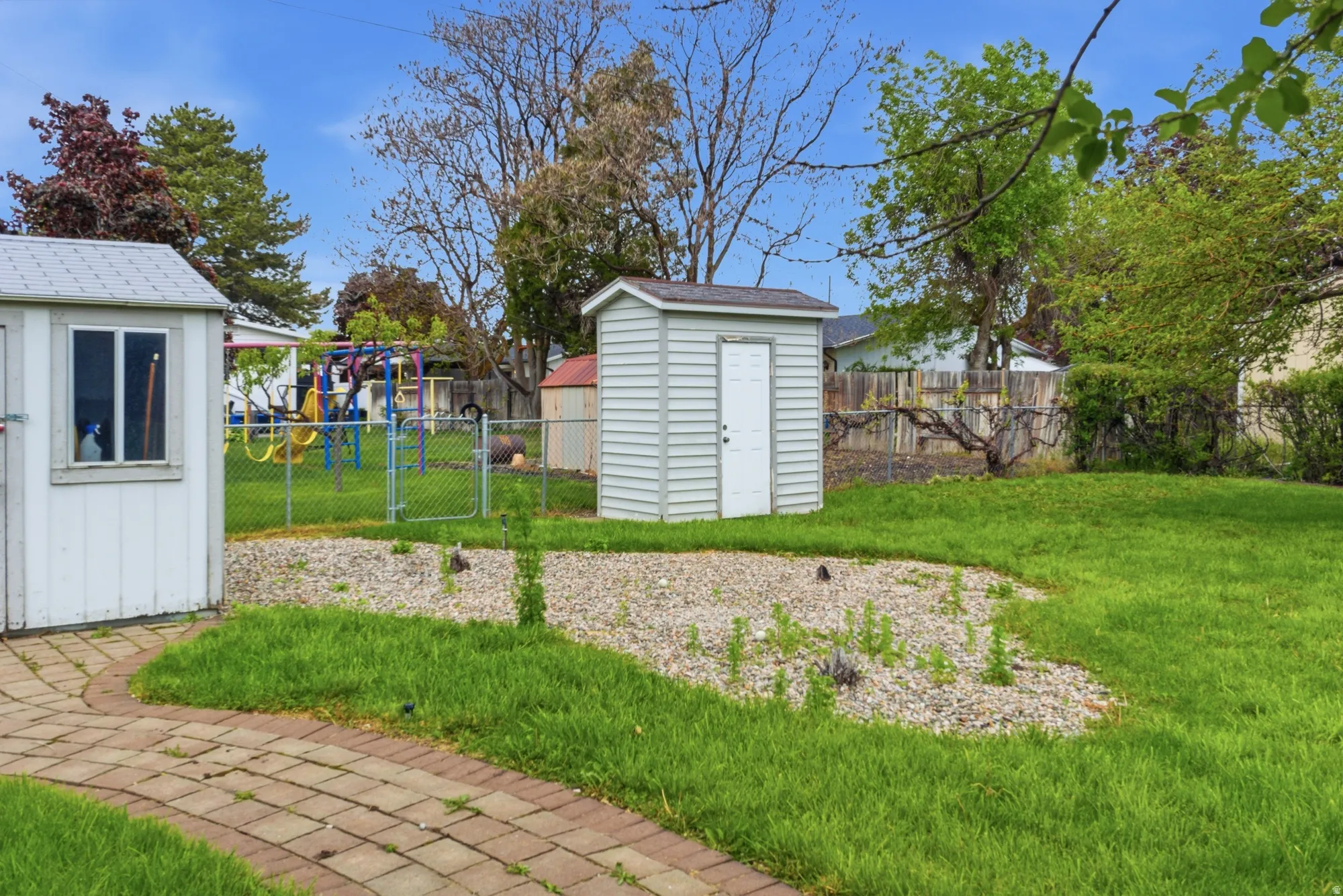 Expansive backyard featuring a brick paver pathway, a gravel-covered area, and two detached storage sheds