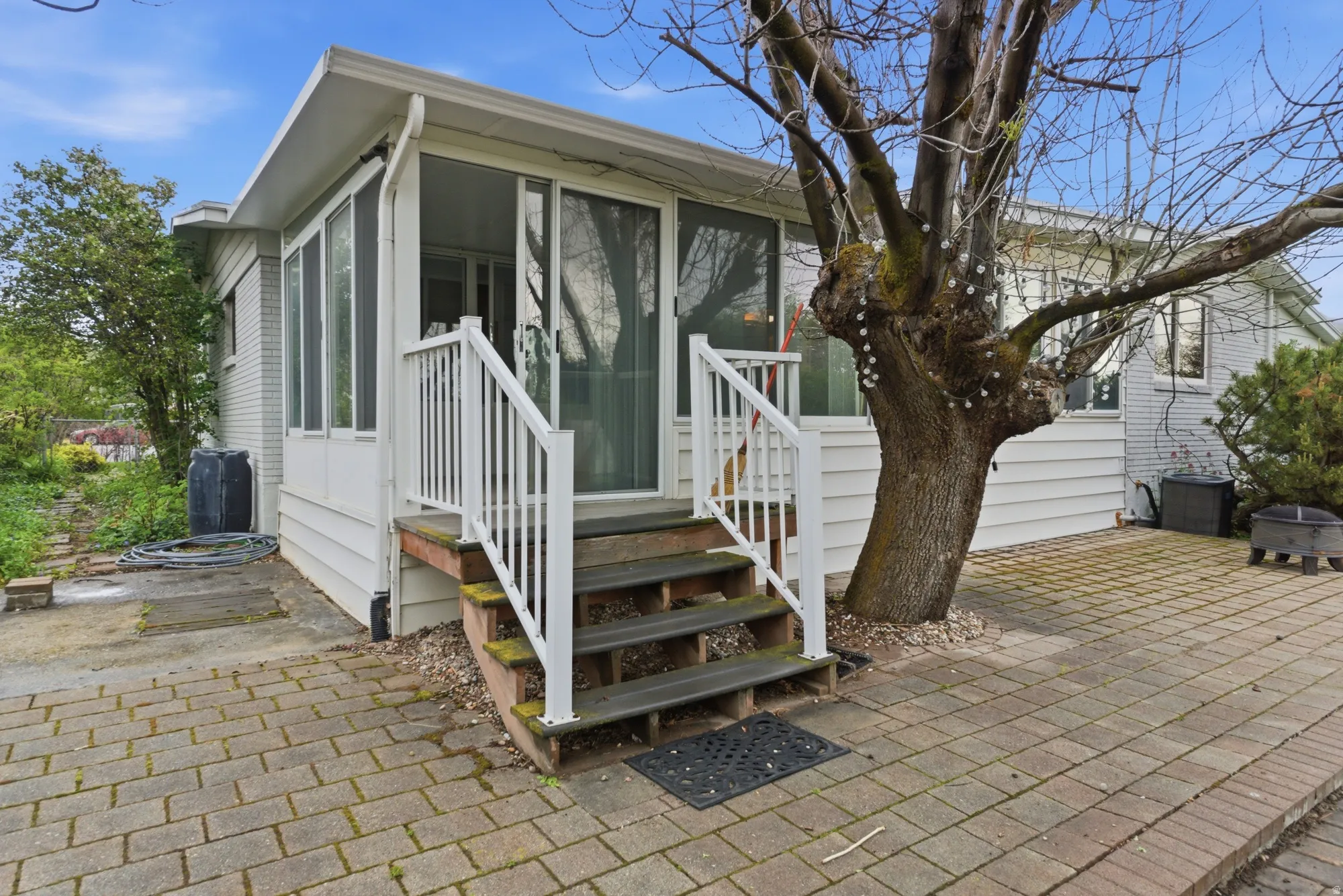 Screened porch with sliding glass door entry, leading to a paver patio with a mature tree