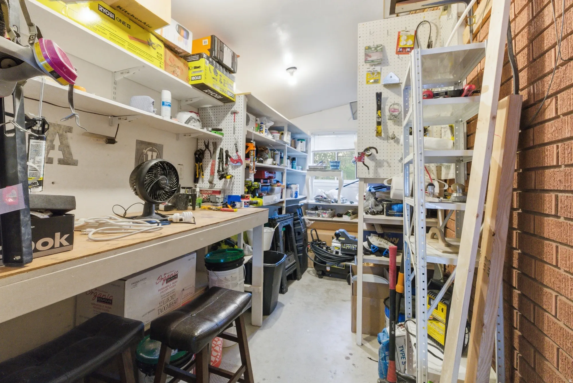 Dedicated workshop space featuring extensive shelving, a durable workbench, pegboard storage, and a single window for natural light
