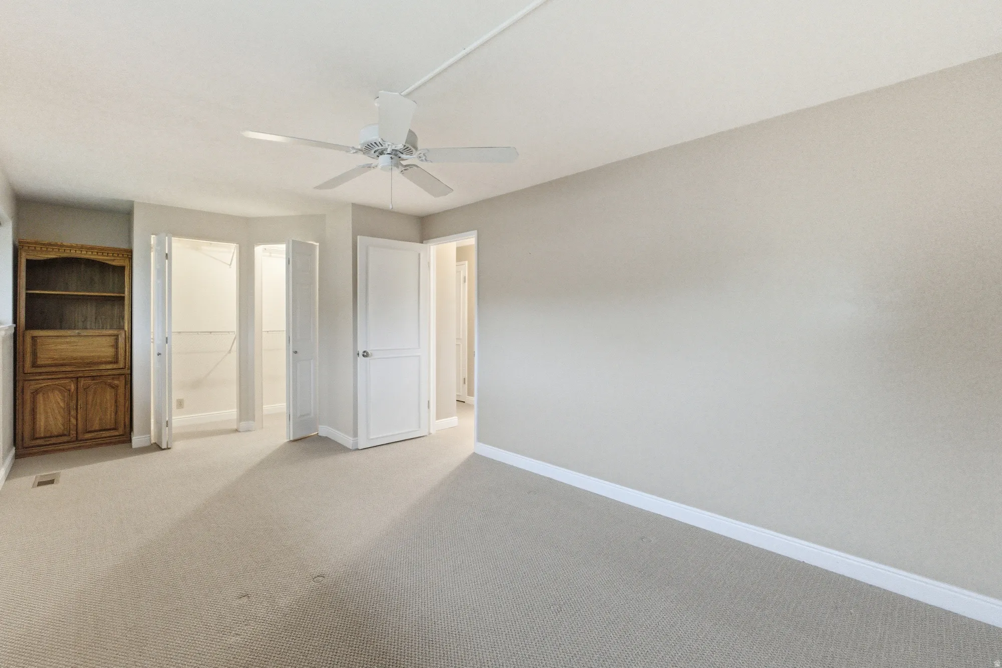Spacious room featuring neutral carpeting, light-toned walls, and a ceiling fan with integrated lighting