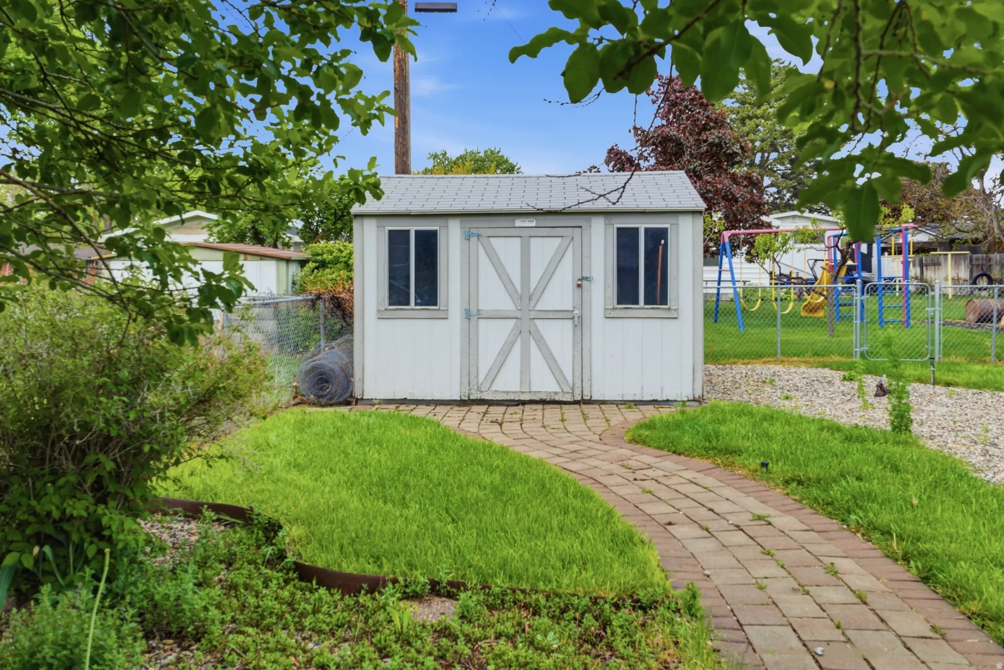 Detached storage shed with two windows and a gray-painted door, featuring a metal roof