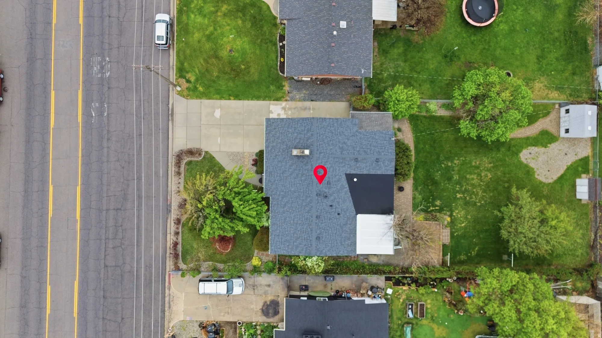 Property featuring a dark gray asphalt shingle roof, a paved driveway, and a front yard with mature landscaping