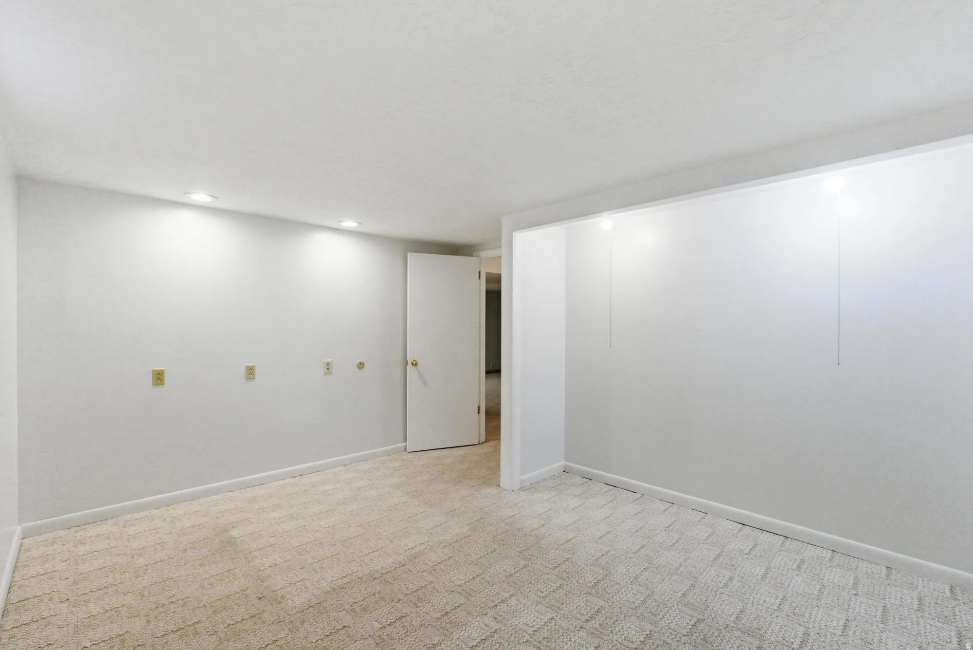 Recessed ceiling lighting illuminates a spacious room featuring light-colored wall-to-wall carpeting