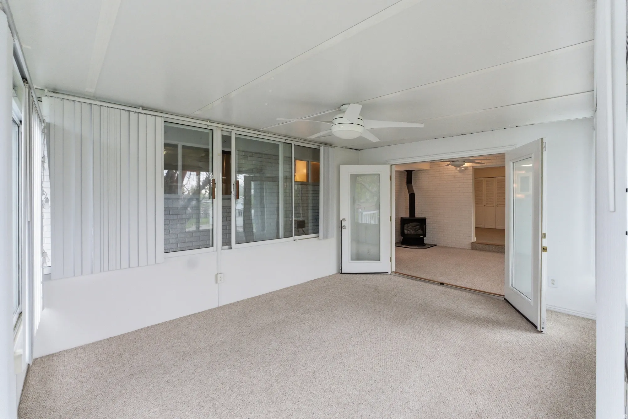 Enclosed sunroom featuring light-colored carpeting, a ceiling fan, and multiple large windows with vertical blinds