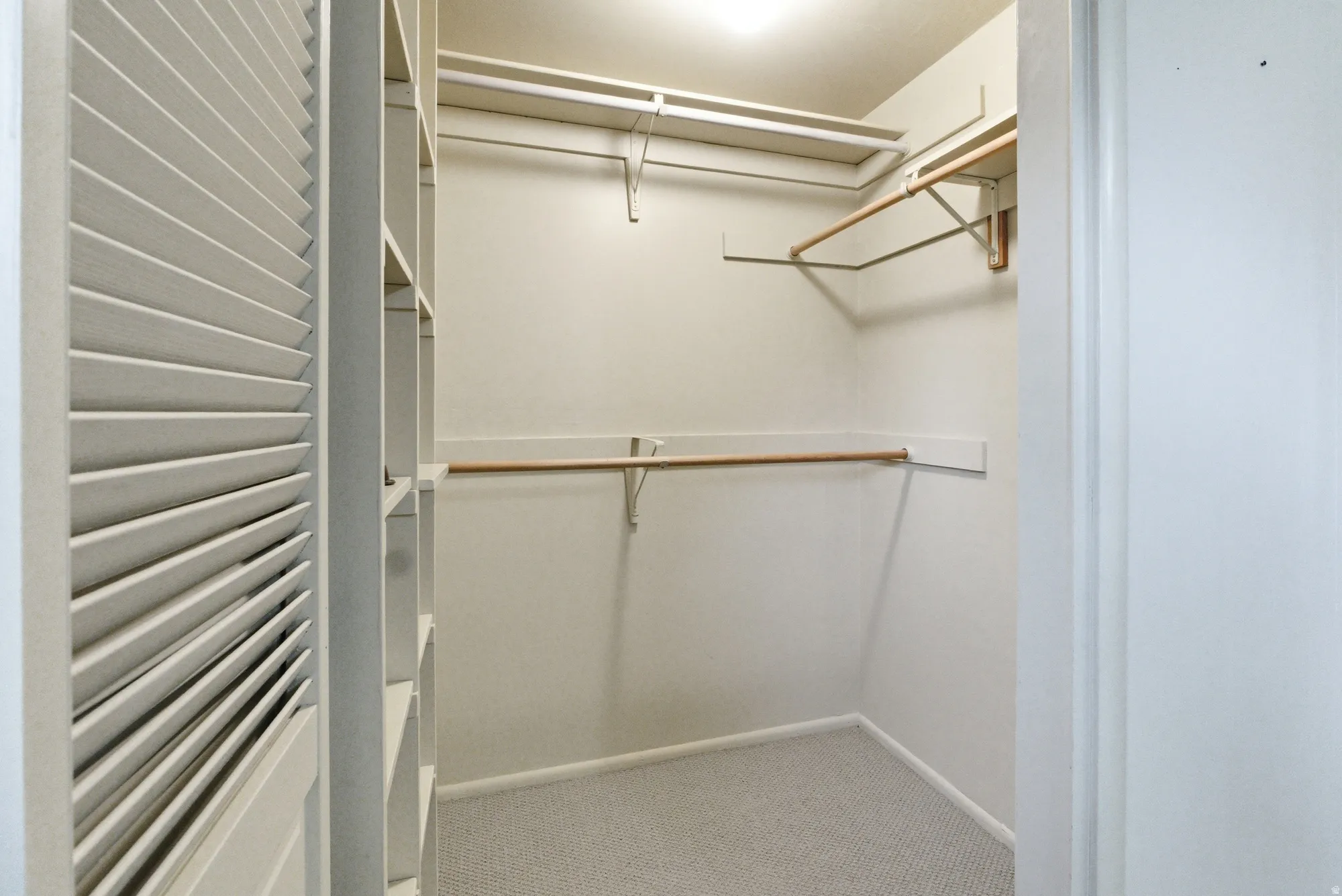 Walk-in closet with carpet flooring, louvered bi-fold doors, built-in shelving, and multiple hanging rods