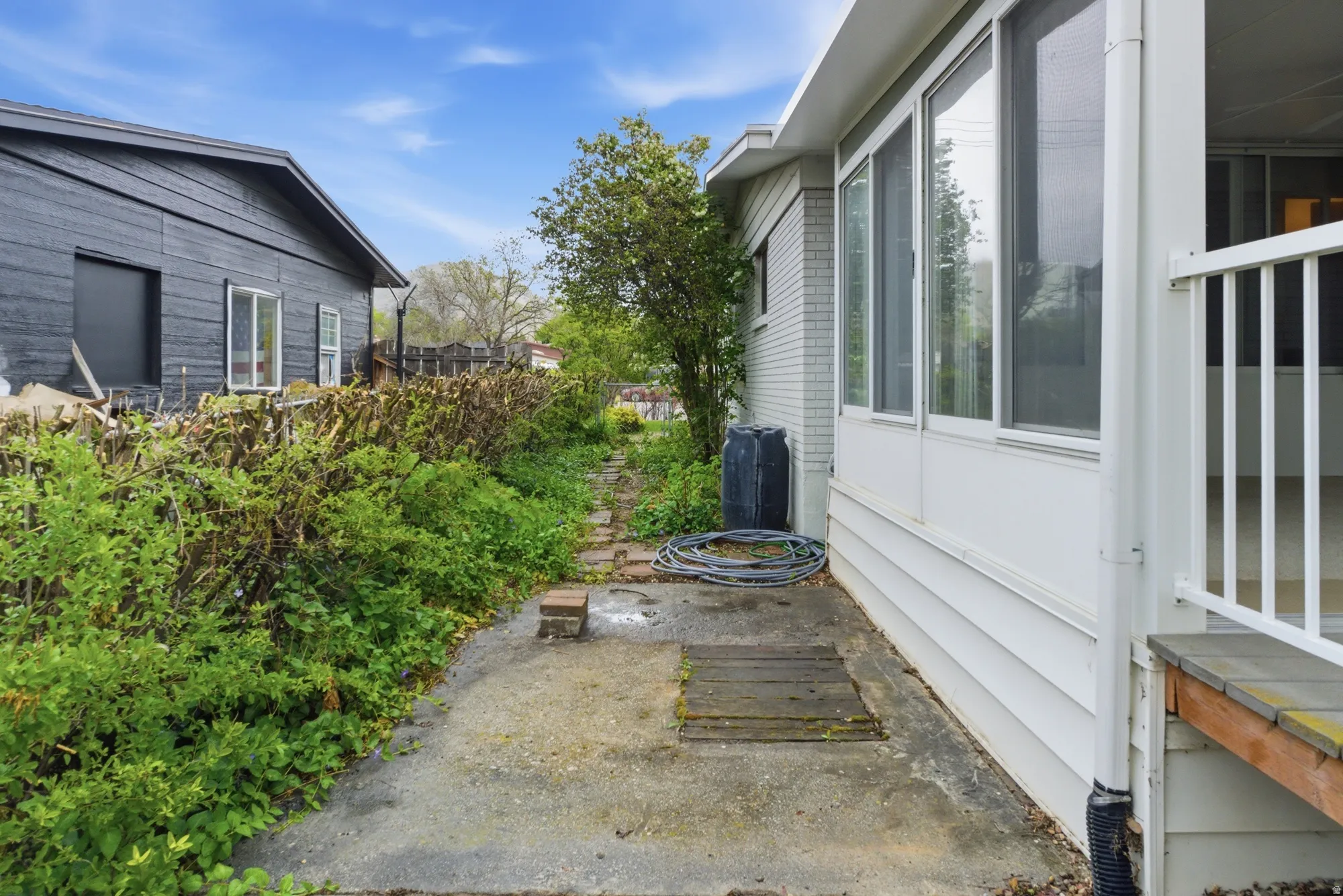 Side patio area featuring concrete and wood-finish stepping stones, flanked by established hedges