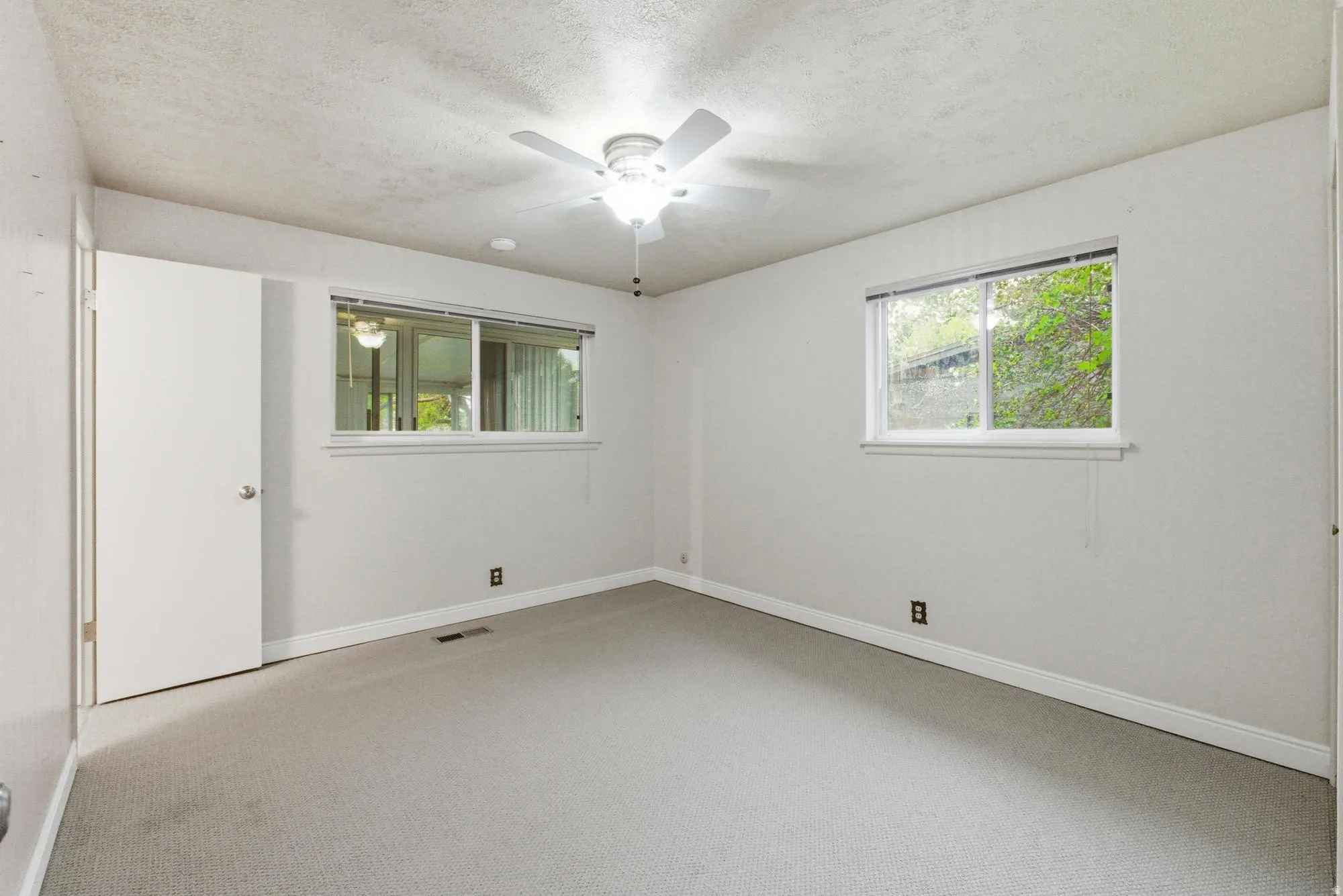 Carpeted interior space featuring two windows with horizontal blinds, a ceiling fan with integrated lighting, and a white interior door