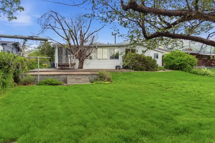 Expansive rear yard featuring a verdant lawn and a raised block patio with steps