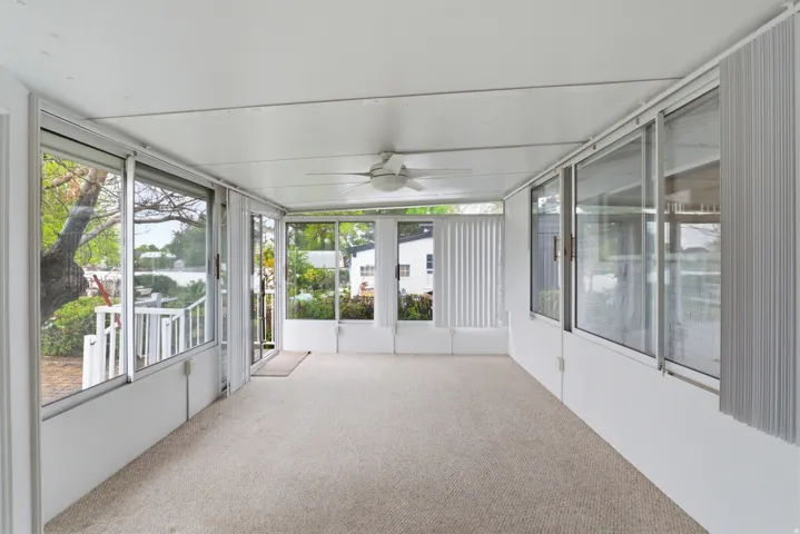 Enclosed patio featuring light-colored carpeting, white paneled walls, and a white ceiling with a ceiling fan