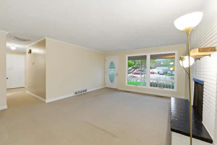Carpeted room with a white brick fireplace and a dark mantel