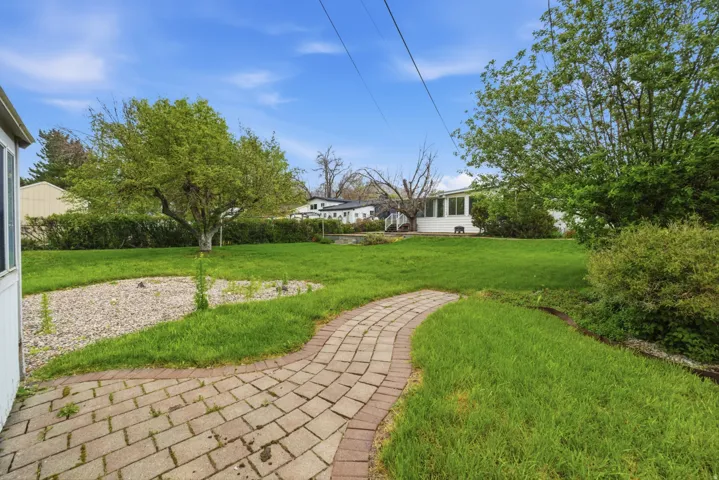 Expansive rear yard featuring a paved brick pathway, a large mature tree, established green lawn, and a decorative gravel bed