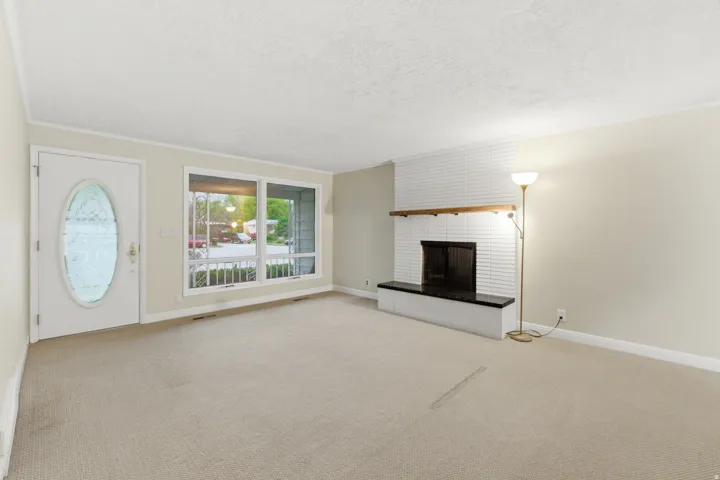 Living space featuring a white brick fireplace with a wood mantle, a dark hearth, and a light-colored carpet
