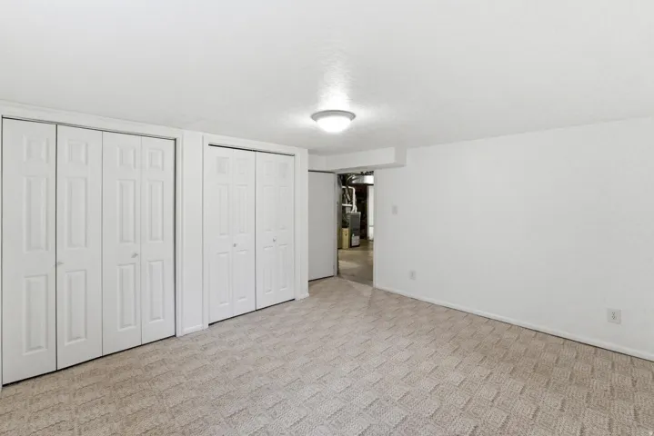 Carpeted room featuring multiple bifold closet doors, a flush-mount ceiling light fixture, and white painted walls