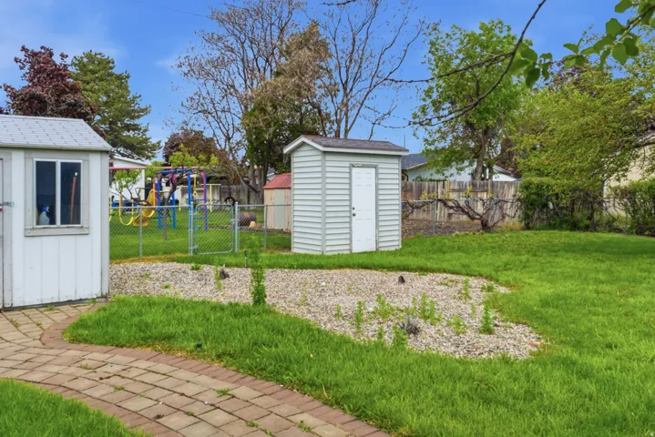 Expansive backyard featuring a brick paver pathway, a gravel-covered area, and two detached storage sheds