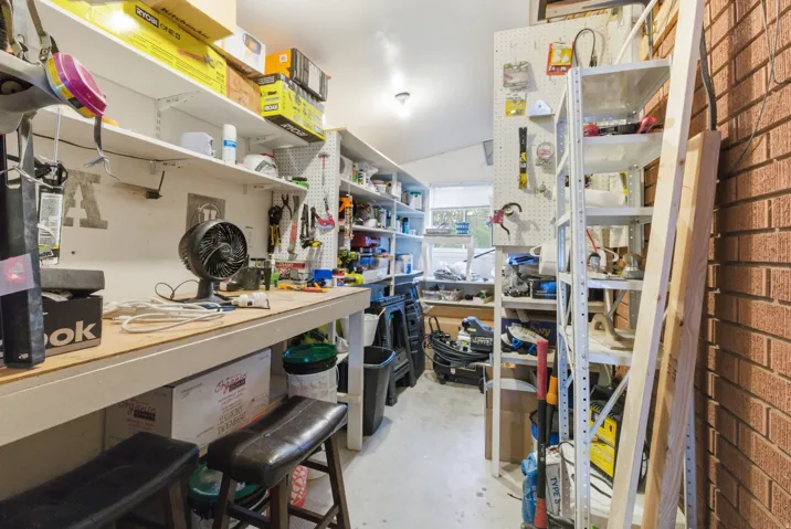 Dedicated workshop space featuring extensive shelving, a durable workbench, pegboard storage, and a single window for natural light