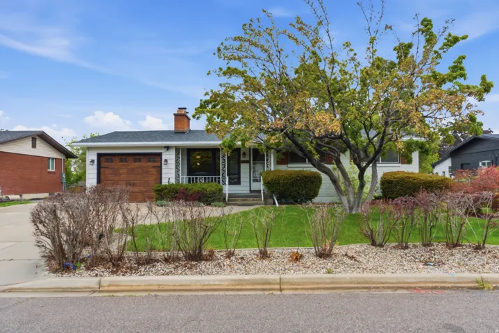 Single-story residence featuring a wood-finish garage door, a prominent brick chimney, and a dark shingle roof