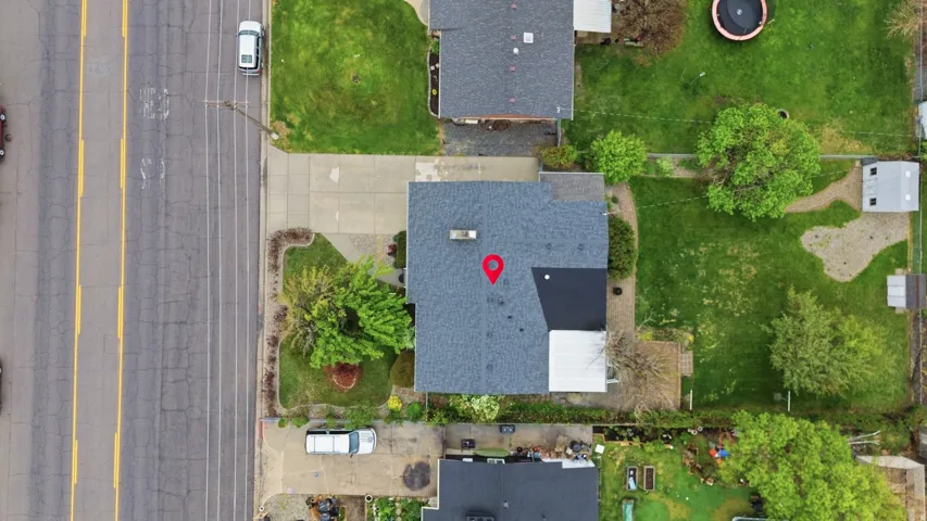Property featuring a dark gray asphalt shingle roof, a paved driveway, and a front yard with mature landscaping