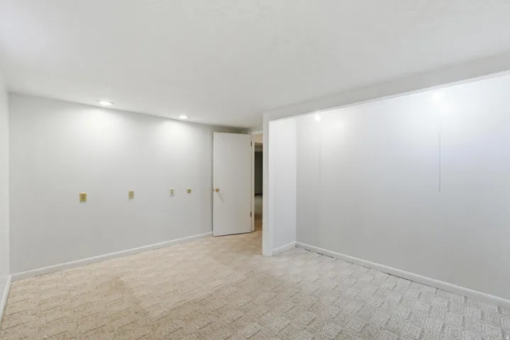 Recessed ceiling lighting illuminates a spacious room featuring light-colored wall-to-wall carpeting