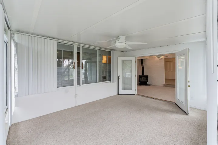 Enclosed sunroom featuring light-colored carpeting, a ceiling fan, and multiple large windows with vertical blinds