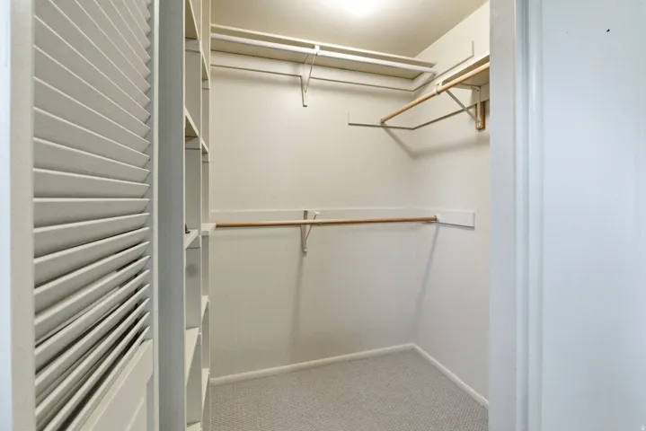 Walk-in closet with carpet flooring, louvered bi-fold doors, built-in shelving, and multiple hanging rods