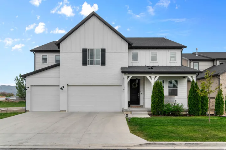 Modern farmhouse exterior featuring white siding and black accents, a covered front porch, a two-car garage, and a concrete driveway