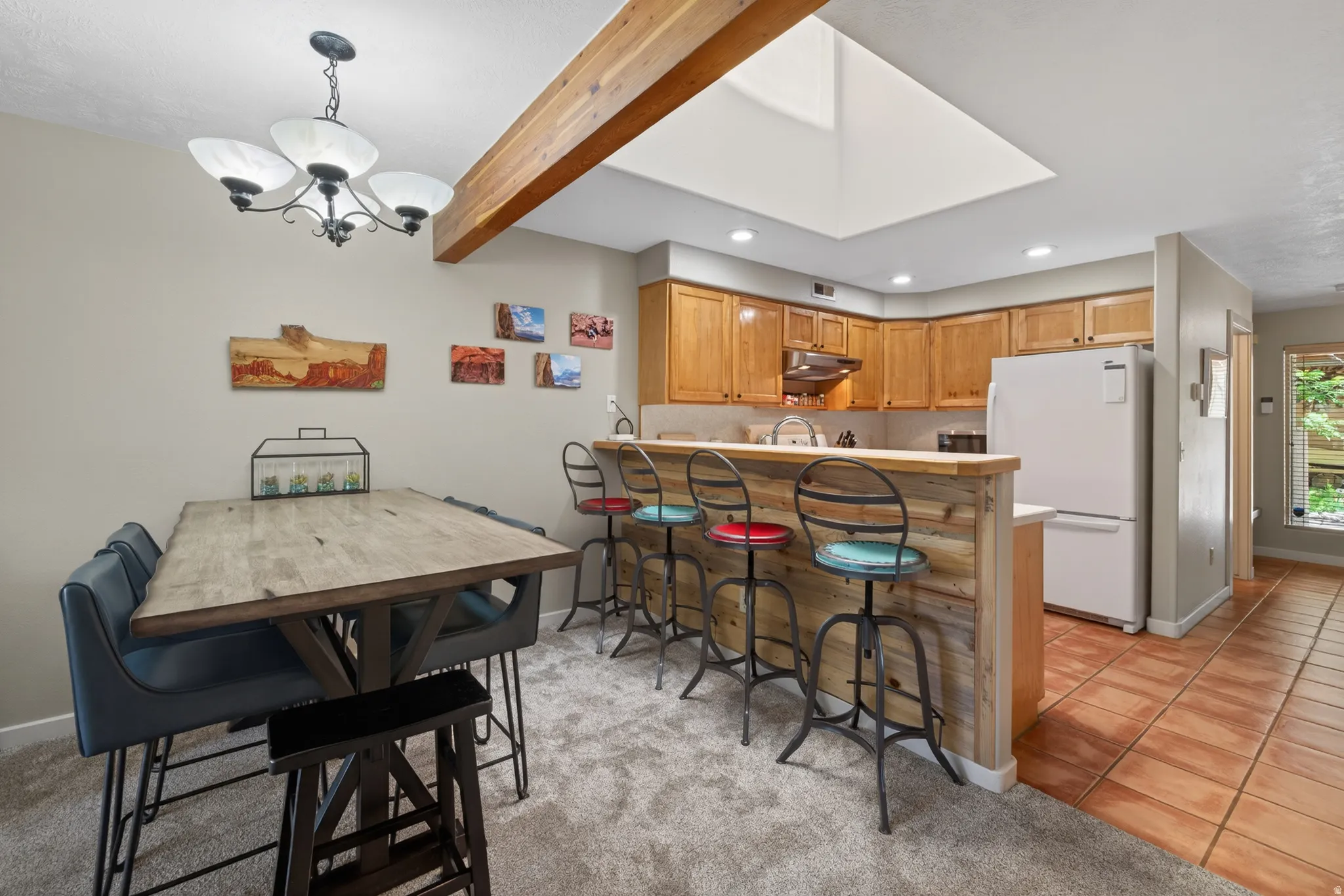 Open-concept kitchen and dining area featuring a breakfast bar with a wood-finish facade, recessed lighting, a skylight, and wood cabinetry