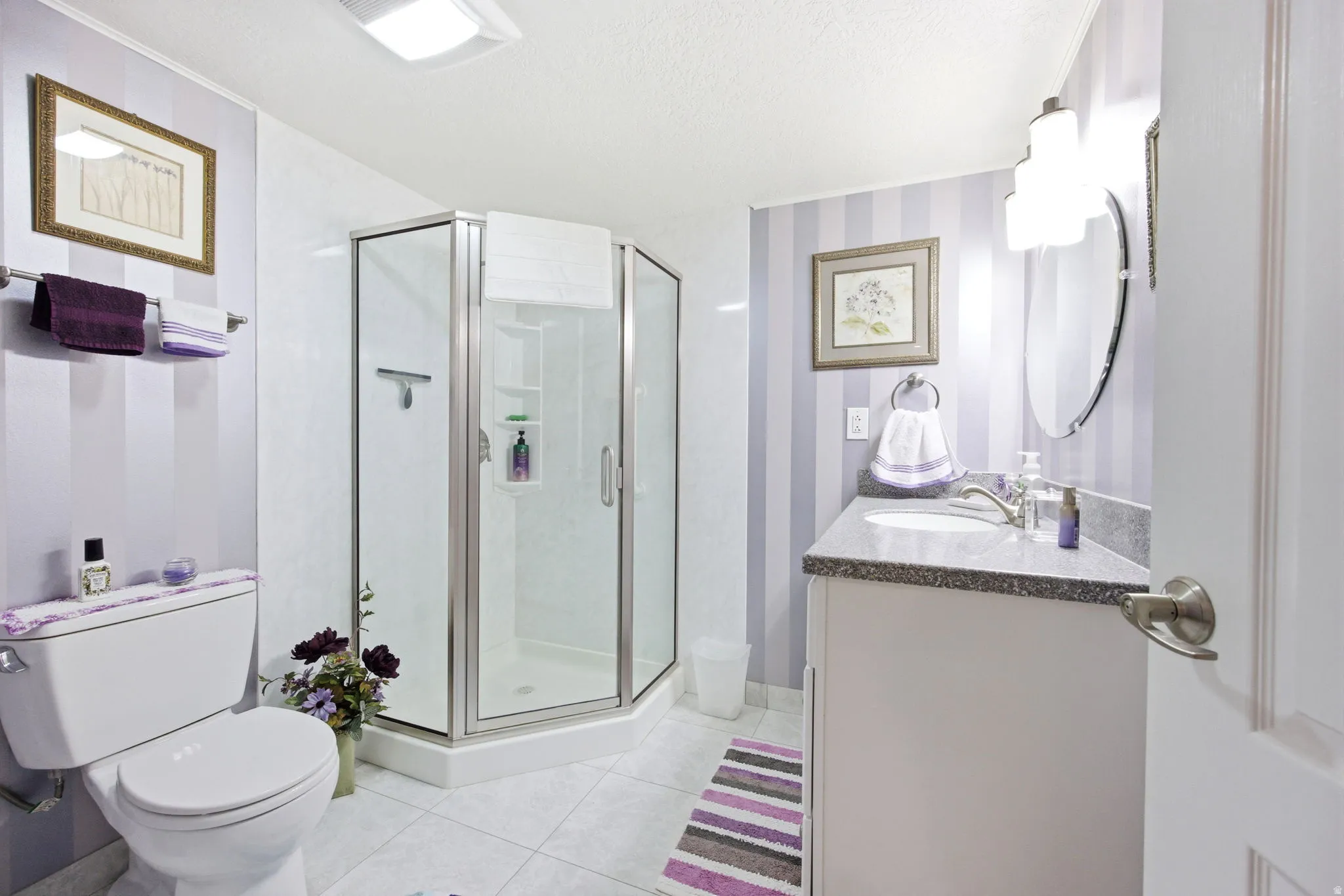 Full bathroom featuring a corner shower with glass enclosure, white vanity with stone countertop, oval vanity mirror, and white toilet